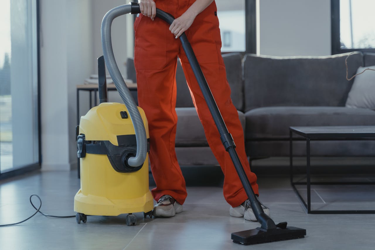 services-01 A professional cleaner in red coveralls vacuums a contemporary living room with a yellow vacuum cleaner.