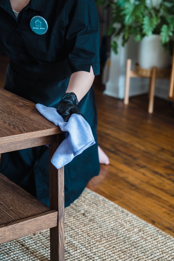 about-04 Person in uniform cleaning a wooden table indoors with a cloth.